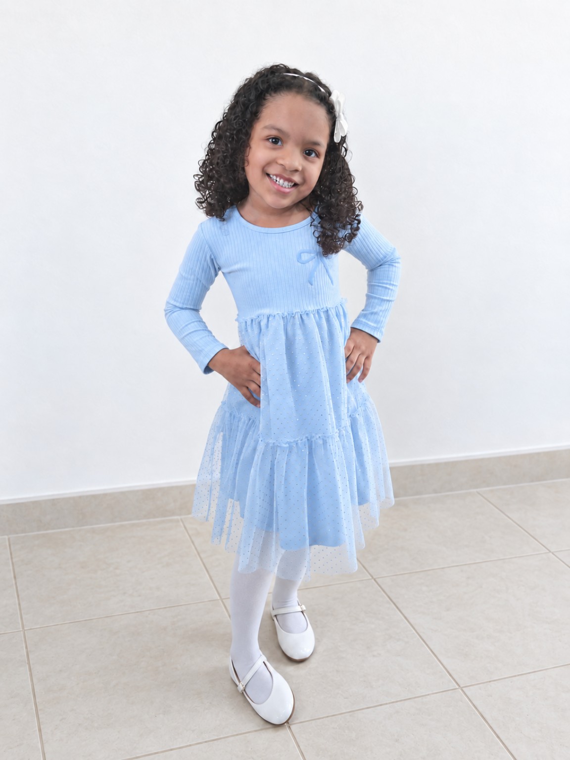 Camilly de corpo inteiro com vestido azul-claro, meia-calça e sapatos brancos